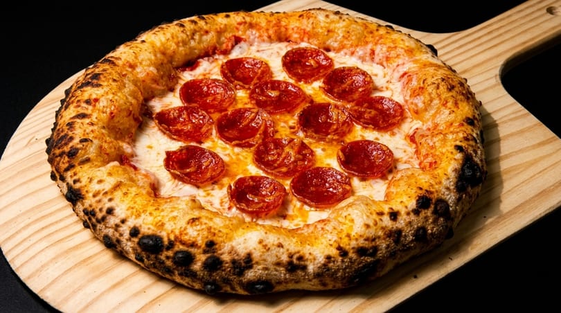 A freshly baked pepperoni pizza with a bubbly crust, served on a wooden pizza peel.