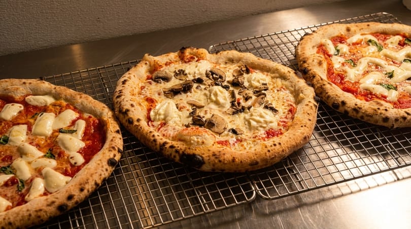 Three freshly baked pizzas, one with mushrooms, cooling on a wire rack.