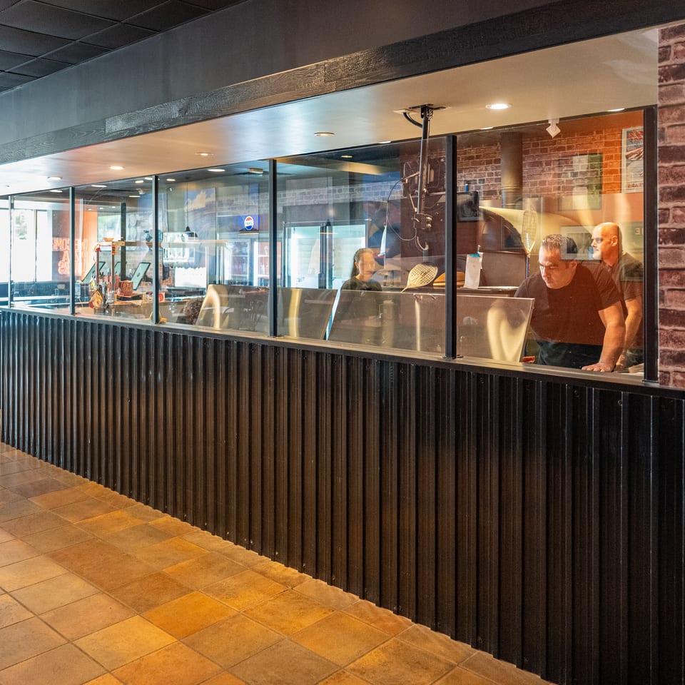 Restaurant interior with a glass-enclosed kitchen area where staff are preparing food.