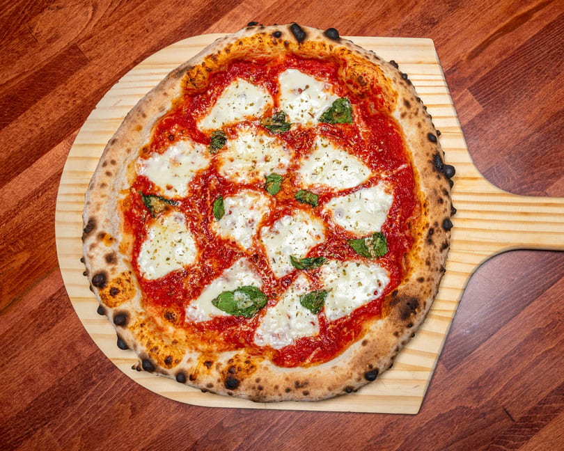 Neapolitan Margherita pizza with fresh mozzarella, basil, and tomato sauce on a wooden peel.