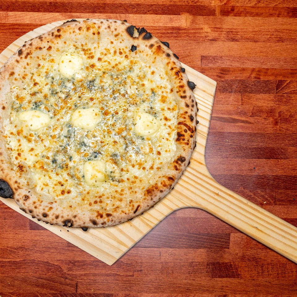 Four cheese pizza with a crispy crust and melted cheese on a wooden pizza peel.