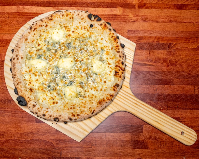 Four cheese pizza with a crispy crust and melted cheese on a wooden pizza peel.
